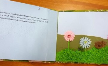 Una fiaba su un libro tattile: a sinistra la pagina con il testo. A destra le illustrazioni tattili con un prato fiorito, fiori e una farfalla colorata