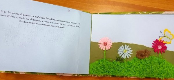 Una fiaba su un libro tattile: a sinistra la pagina con il testo. A destra le illustrazioni tattili con un prato fiorito, fiori e una farfalla colorata
