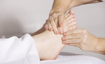 Le mani di un fisioterapista massaggiano il piede di una paziente distesa sul lettino