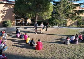 I bambini della scuola elementare di Macerata sono seduti in circoli nel giardino dell'Istituto, in una bella giornata di sole. Stefania Terrè, il suo Italo e le insegnanti sono in piedi davanti ai piccoli