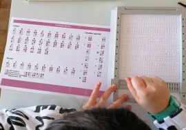 Le mani di una bambina delle elementari incidono su un foglio i caratteri del braille con l'aiuto della tavoletta e di un punteruolo