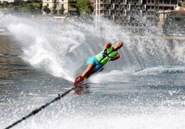 Il campione paralimpico Daniele Cassioli durante una bellissima evoluzione mentre pratica sci d'acqua. Indossa una tuta verde, è trainato da una imbarcazione e alle sue spalle lascia una scia d'acqua simile a un'onda