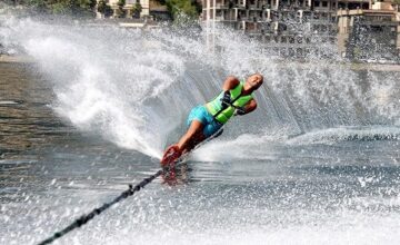 Il campione paralimpico Daniele Cassioli durante una bellissima evoluzione mentre pratica sci d'acqua. Indossa una tuta verde, è trainato da una imbarcazione e alle sue spalle lascia una scia d'acqua simile a un'onda