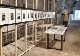 Un settore della bella mostra proposta da Ancona foto festival. A ridosso di una parete, all'interno della Mole, sono esposte le foto in successione sistemate su cavalletti color legno. Sul fondo un fotografo riprende l'allestimento