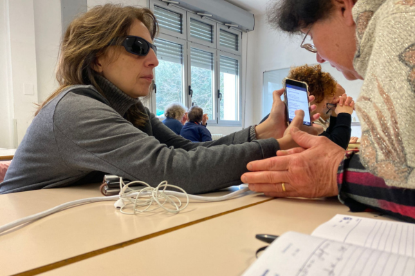 Nella foto un momento di una lezione di tecnologia assistiva. In primo piano, sedute a una scrivania, la presidente Uici di Ascoli, Gigliola Chiappini, mostra la schermata di cellulare a una socia