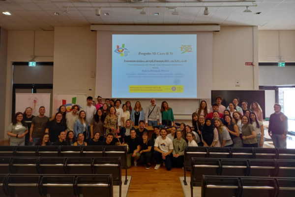 Una bella foto di gruppo all'interno della grande aula dell'università. In primo piano i banchi, in fondo, davanti alla scrivania, gli studenti, gli insegnanti e i dirigente Uici posano sorridenti