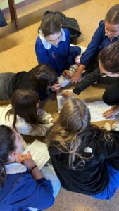 I piccoli studenti della scuola primaria, in grembiule blu e colletto bianco, seduti in circolo sul pavimento scrivono sulle tavolette i caratteri Braille